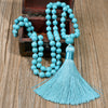 Long turquoise bead necklace with a large blue tassel resting on a wooden surface