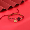 Close-up of a red braided bracelet with a dark red flower charm and a gold circular pendant on a red background.