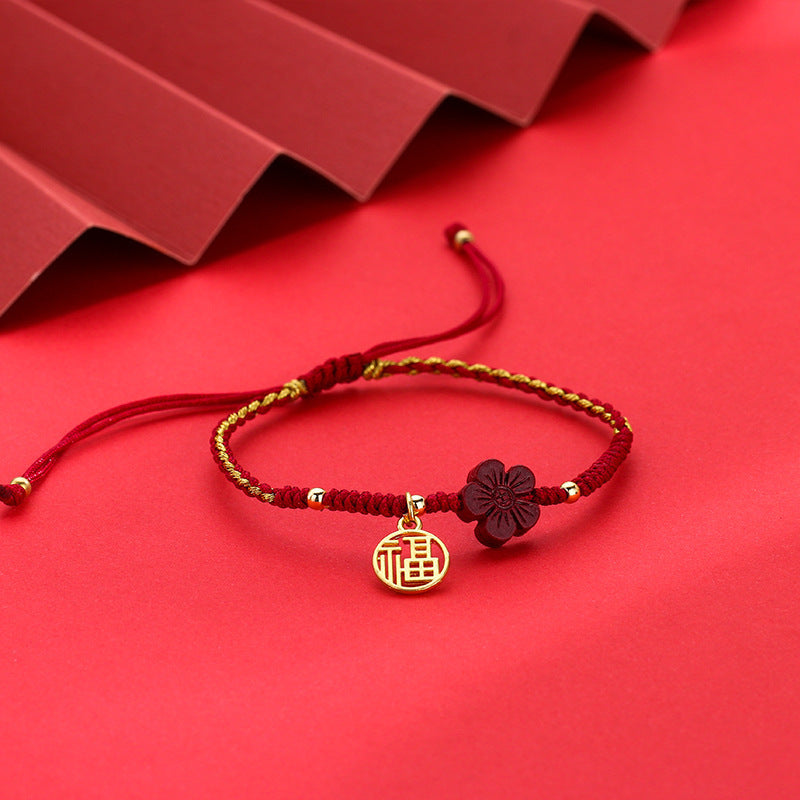 Close-up of a red braided bracelet with a dark red flower charm and a gold circular pendant on a red background.