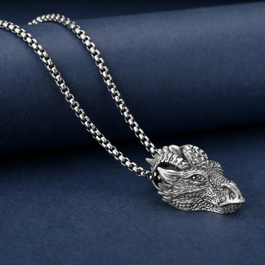 Close up of a silver tone dragon head pendant on a metal chain against a blue background