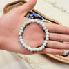 A hand holding a light green ceramic bead bracelet with a stretch cord