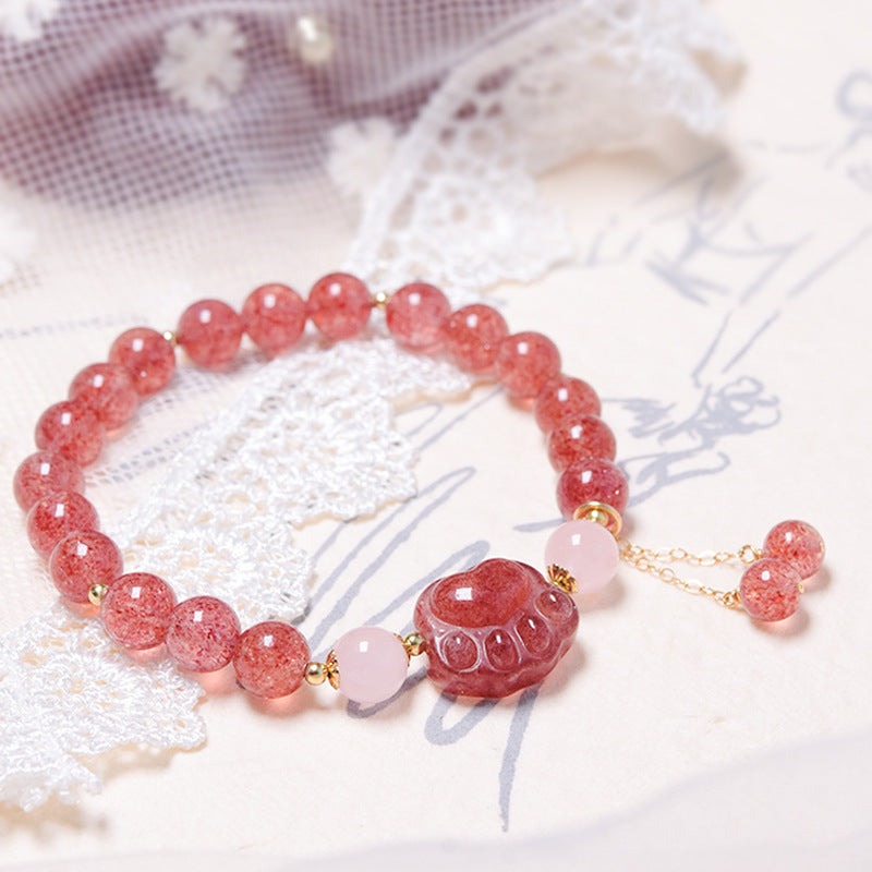 Pink strawberry quartz beaded bracelet with a red cat paw charm on a lace background