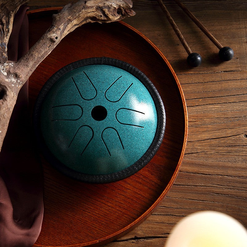 Teal mini steel tongue drum resting on a wooden tray with mallets nearby