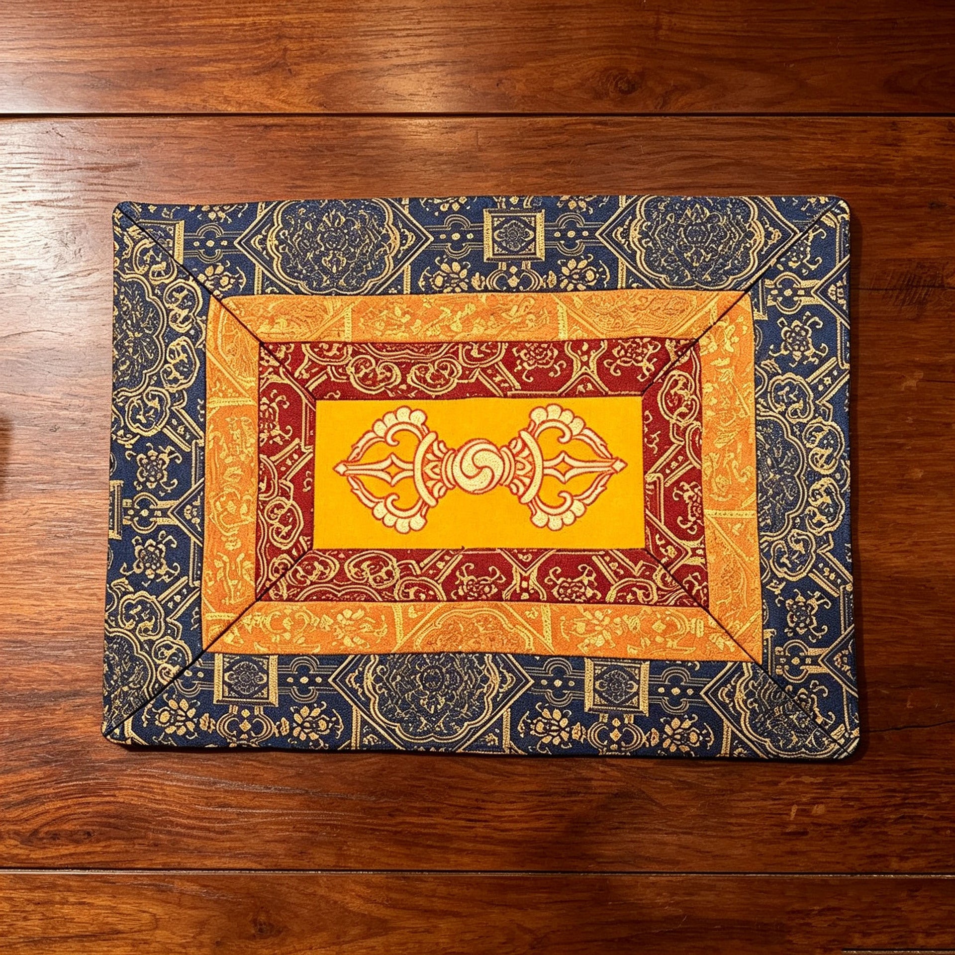 Rectangular embroidered cloth mat with blue patterned border and yellow center featuring gold vajra symbols