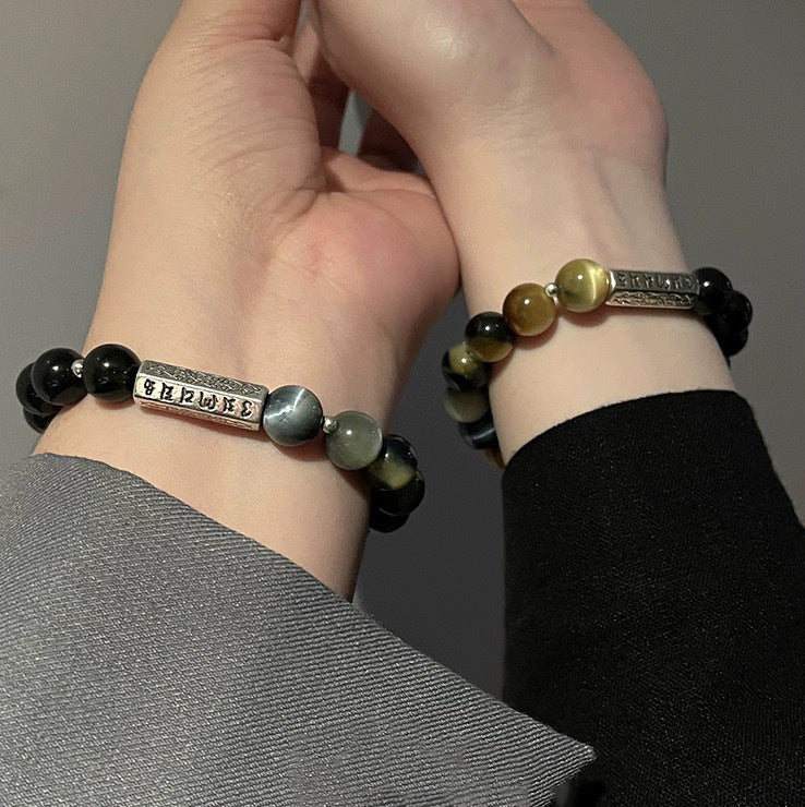 Two wrists wearing matching bracelets with black and yellow tiger eye beads and a silver charm