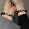 Two wrists wearing matching bracelets with black and yellow tiger eye beads and a silver charm