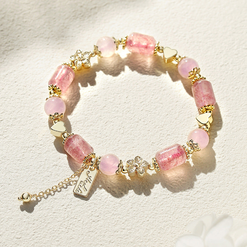 Pink Strawberry Quartz bracelet with gold-tone heart and flower charms on a white background