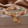 Multi-colored rutilated quartz bracelet with gold charm on a box