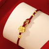 Close up of a red braided cord bracelet with a gold flower charm on a wrist