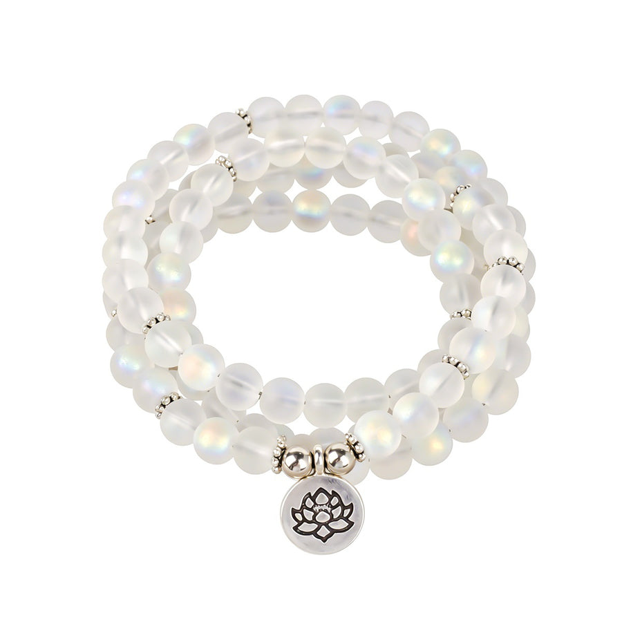 Close up of a white moonstone beaded necklace with a silver lotus pendant on a wooden surface