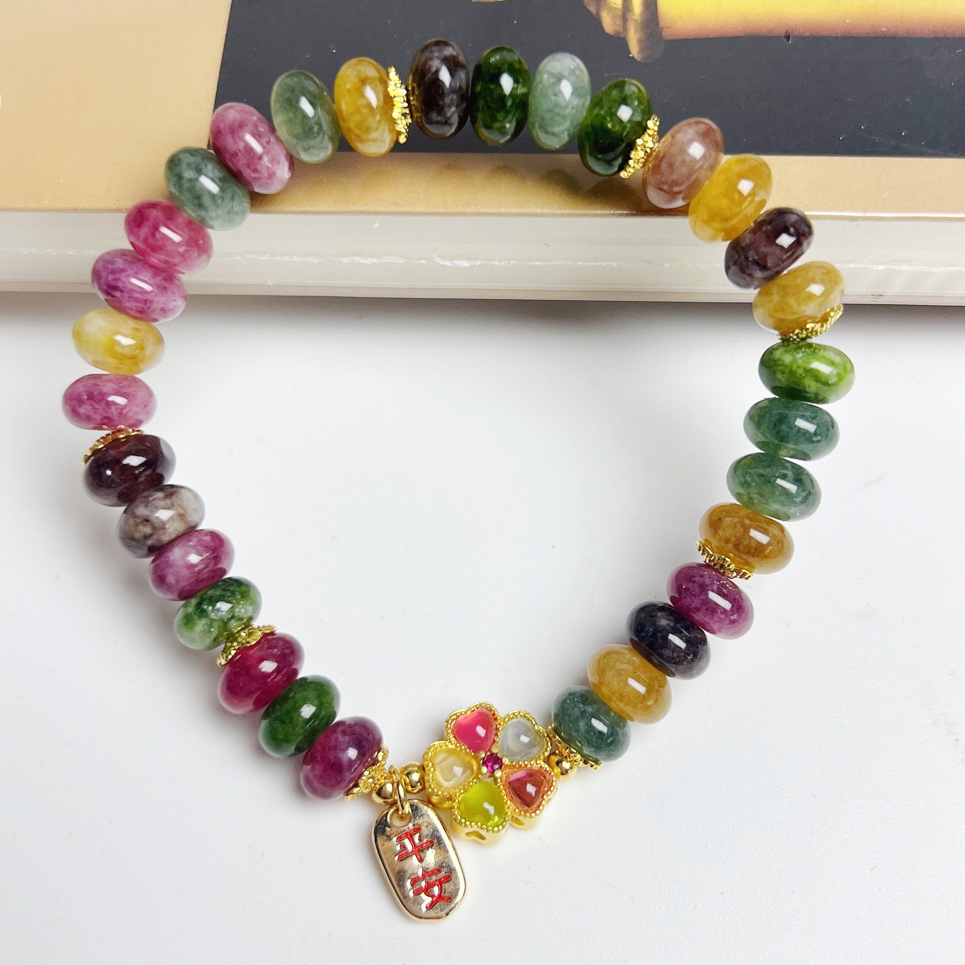 Multi-colored tourmaline bead bracelet with a gold flower charm on a white background