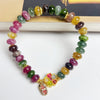 Multi-colored tourmaline bead bracelet with a gold flower charm on a white background