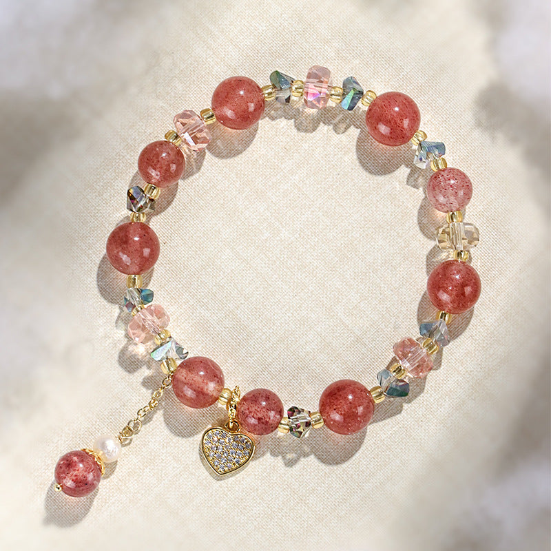 Close-up of a pink strawberry quartz beaded bracelet with a gold heart charm on a white background