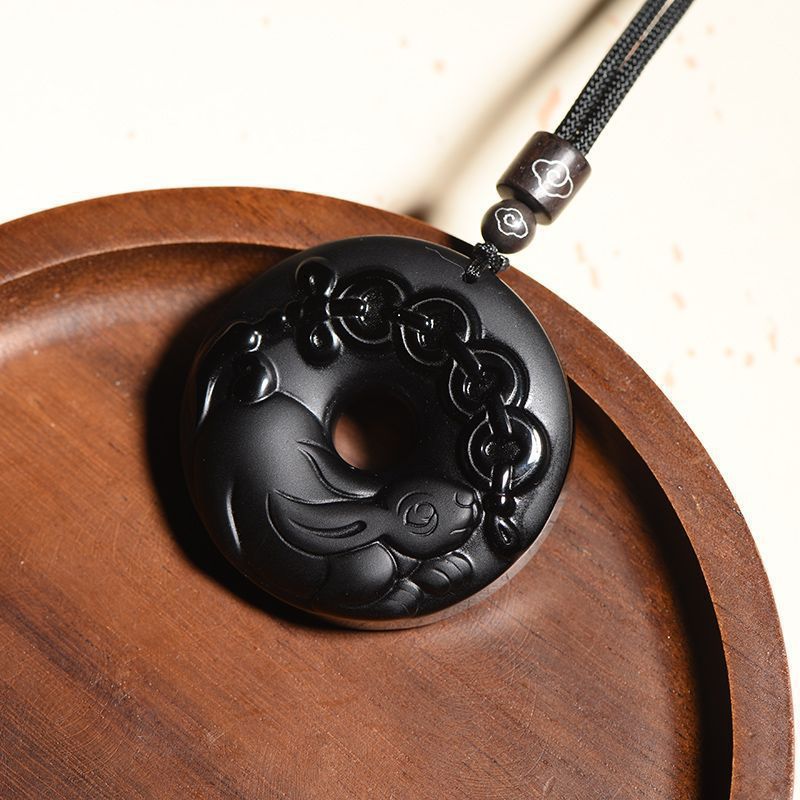 Close up of a carved black obsidian rabbit pendant on a black cord resting on a wooden plate