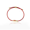 Close-up of a red cord bracelet with a gold-tone koi fish charm