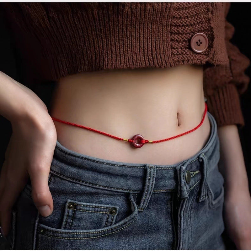 Red velvet waist chain with cinnabar peace buckle worn on bare skin above jeans