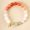 Close up of a beaded bracelet with white and green stones and a gold charm resting on a ceramic cup