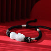 White jade Pixiu bracelet on a black braided cord against a red background