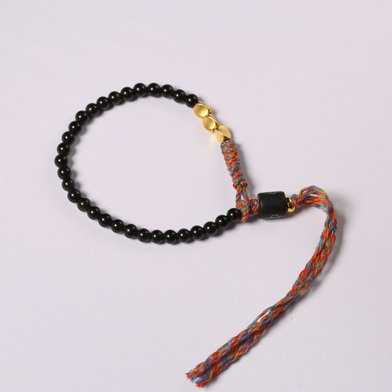 Black obsidian beaded bracelet with a colorful tassel resting on a white plate