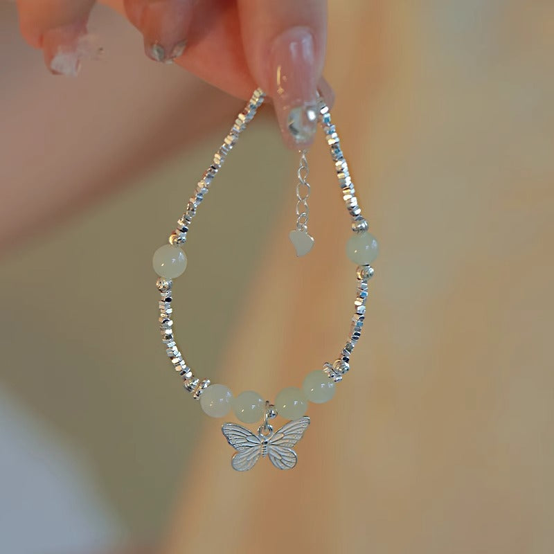 Close up of a silver plated bracelet with a butterfly charm and green beads on a wrist