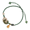 A wrist wearing a green braided bracelet with a jade ring, pearls and a gold bell charm.