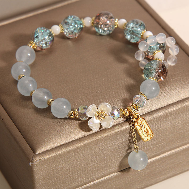 Close up of a beaded bracelet with blue and purple stones and a white flower charm on a box
