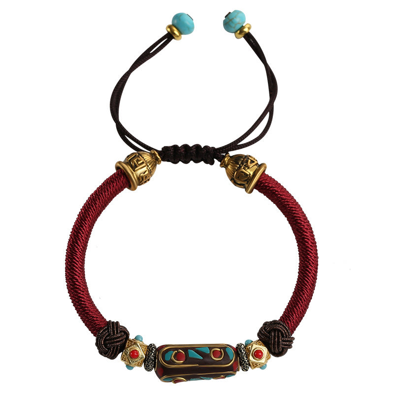 Close up of a red braided bracelet with a central enamel bead worn on a wrist.
