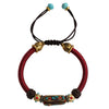 Close up of a red braided bracelet with a central enamel bead worn on a wrist.
