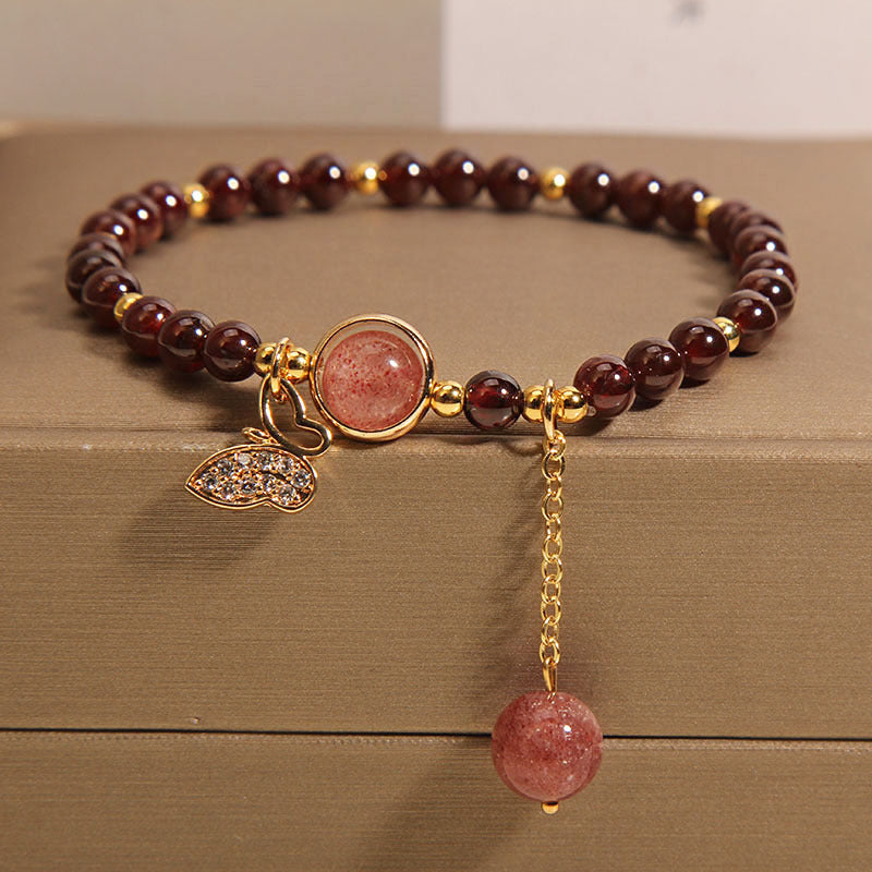Close-up of a red garnet beaded bracelet with a butterfly charm on a wooden surface