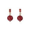 Close up of a woman wearing a red cinnabar drop earring with a gold tone setting