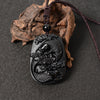 Black obsidian pendant carved with two koi fish and lotus flowers on a brown cord