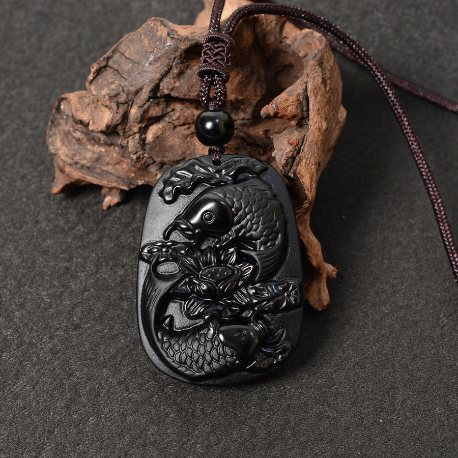 Black obsidian pendant carved with two koi fish and lotus flowers on a brown cord