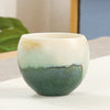 Close up of a green and cream gradient ceramic teacup on a white cloth