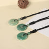 Three Green Aventurine donut pendants on black cords arranged on a beige surface.