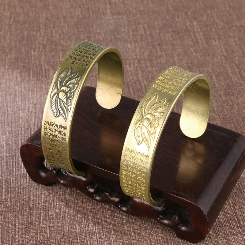 Two brass cuff bracelets with lotus flower and Heart Sutra engraving on a wooden stand