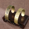 Two brass cuff bracelets with lotus flower and Heart Sutra engraving on a wooden stand