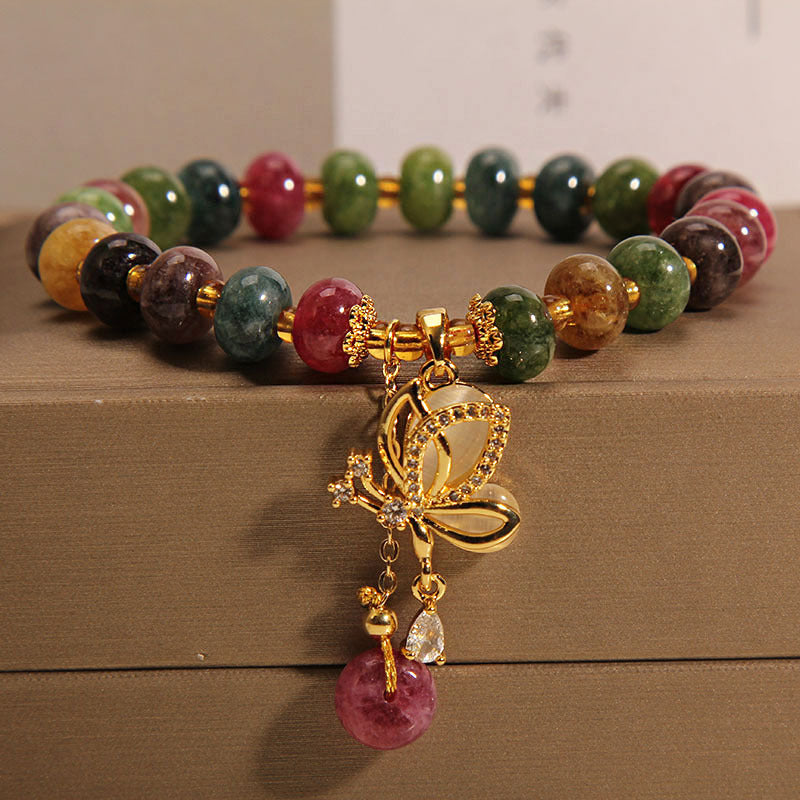 Close up of a colorful tourmaline beaded bracelet with a gold butterfly charm resting on a box