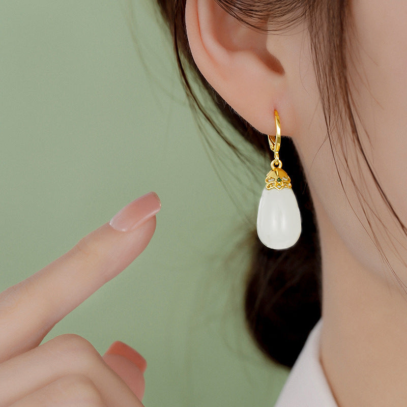 Close up of a white teardrop stone earring on a gold-tone copper post worn on an ear