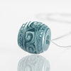 Close up of a carved blue green jade barrel pendant on a silver tone chain