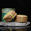 Red metal tin with Tibetan script next to a stack of brown incense coils wrapped in plastic