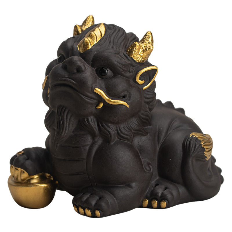 Black purple clay Pixiu tea pet with gold details holding an ingot on a tea mat