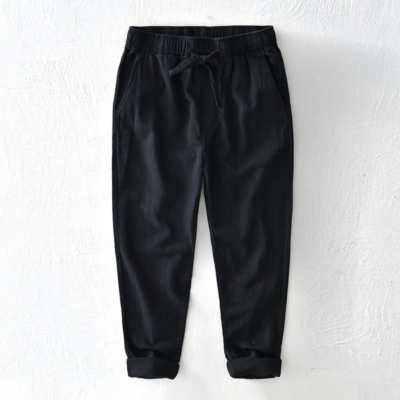 Black men's linen pants with rolled cuffs and drawstring waist on white background