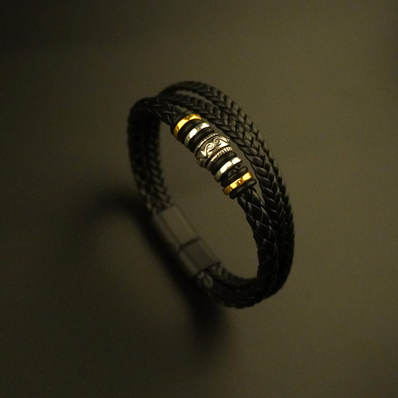 Close up of a black braided leather bracelet with gold and silver alloy beads