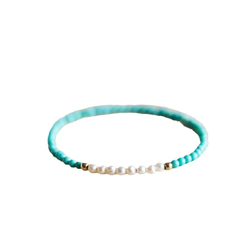 Close up of a thin turquoise and pearl beaded bracelet on a woman's wrist