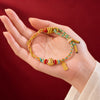 Hand holding a braided red string bracelet with a gold sheep charm