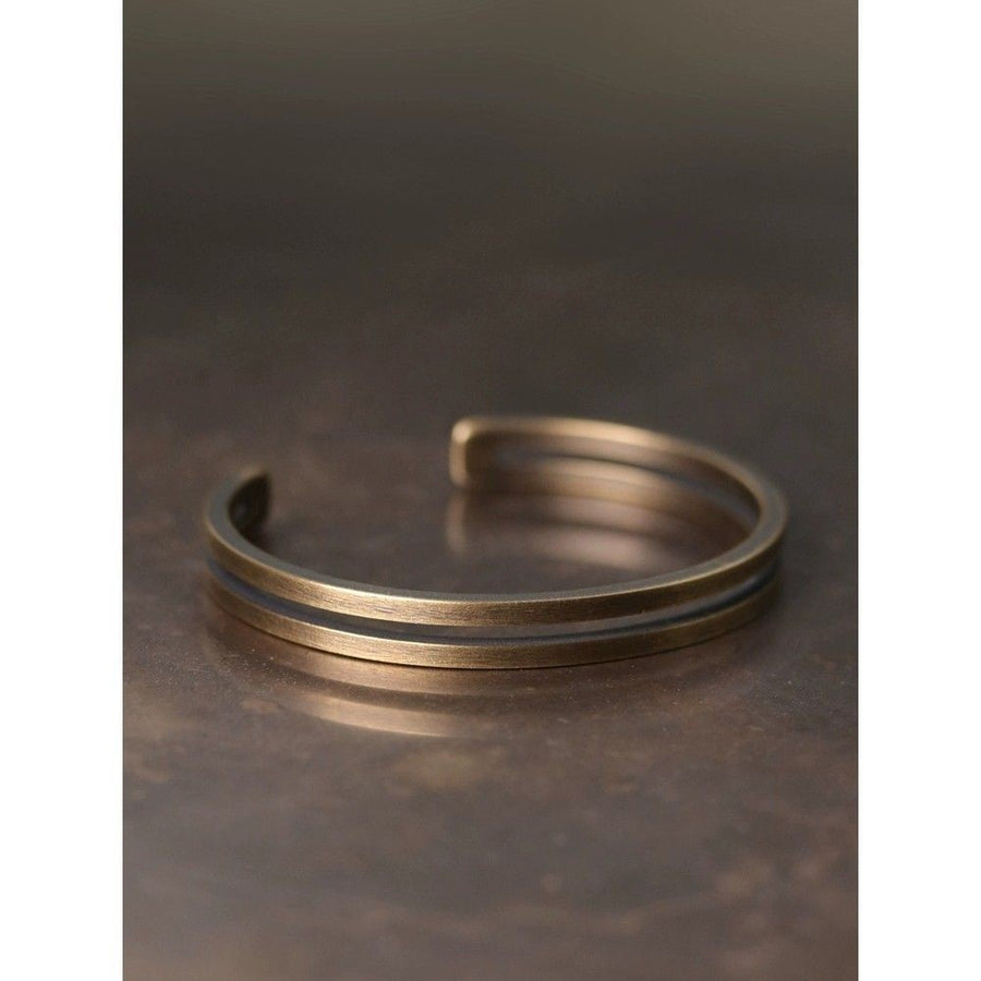 Close up view of a matte brass open cuff bracelet with a textured rope design
