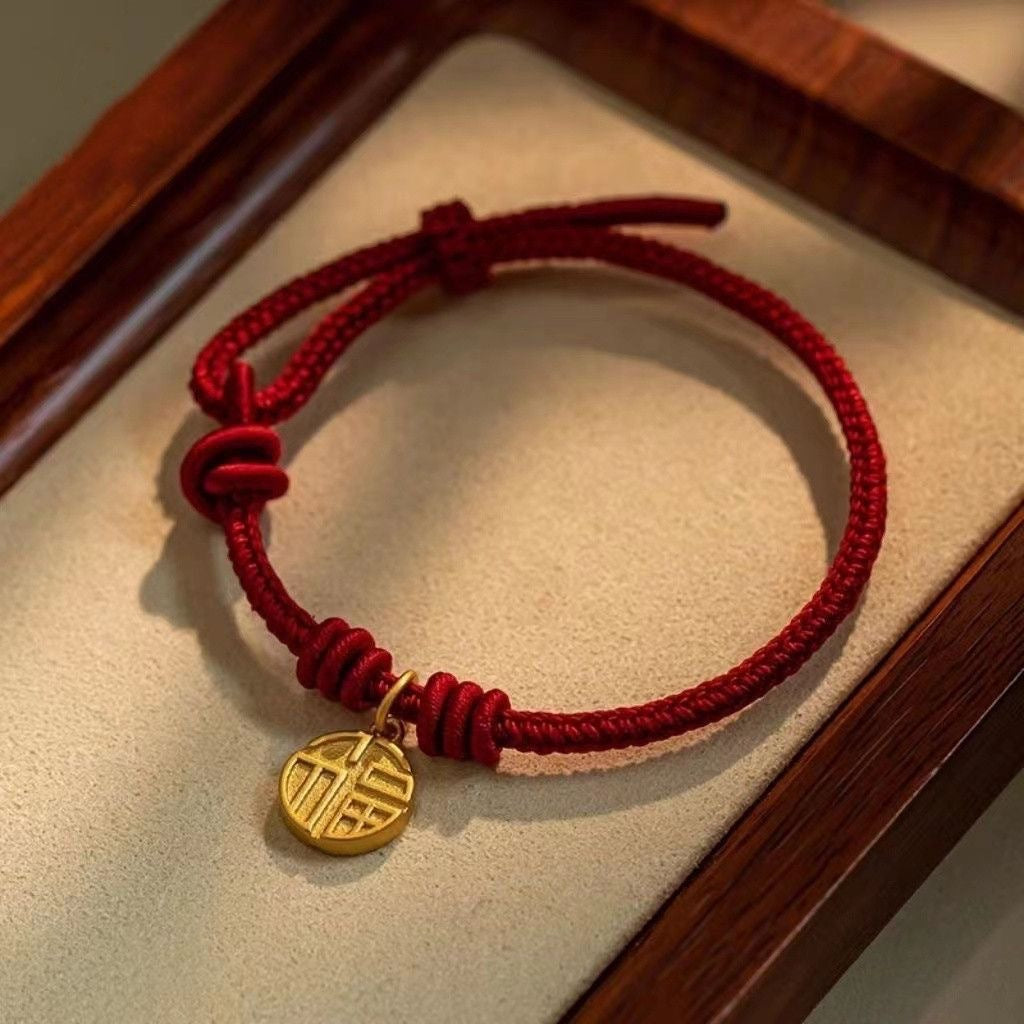 Close-up of a braided red string bracelet with a round gold-tone pendant on a wooden tray