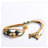Three-strand braided bracelet with green glass beads and gold-tone charms on a white background