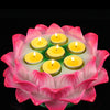 Pink resin lotus flower candle holder with lit yellow tea lights on a green base