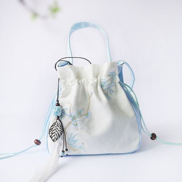 Light blue and white embroidered bucket bag with tassel hanging from drawstring